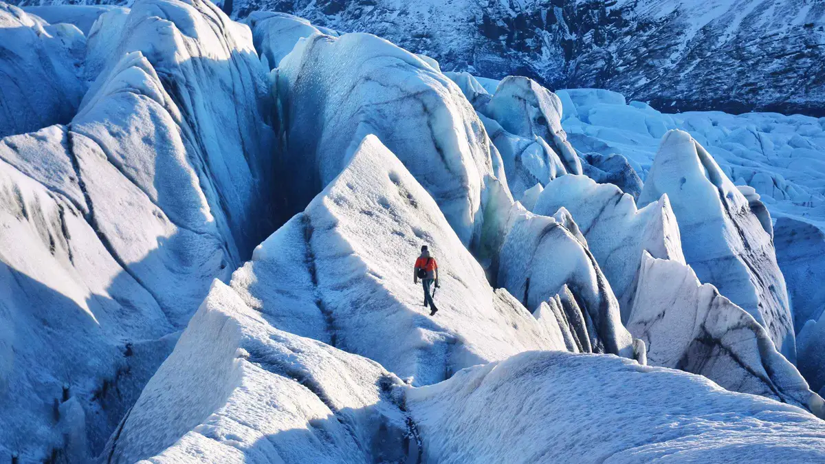Guide pointing out a meltwater sinkhole on a Skaftafell glacier hike beneath the Vatnajökull ice caves, southeast Iceland